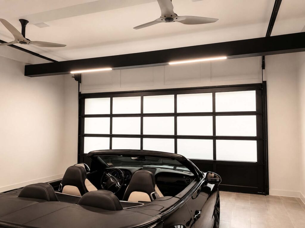 Interior view of a full-light glass garage door in a VAULT luxury garage, showing natural daylight falling across a finished floor and cabinet run.